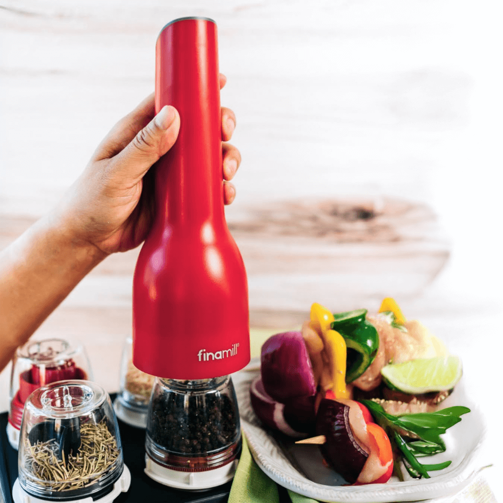 FINAMILL rechargeable grinder in Sangria color, used for grinding spices, with fresh vegetables on a plate.