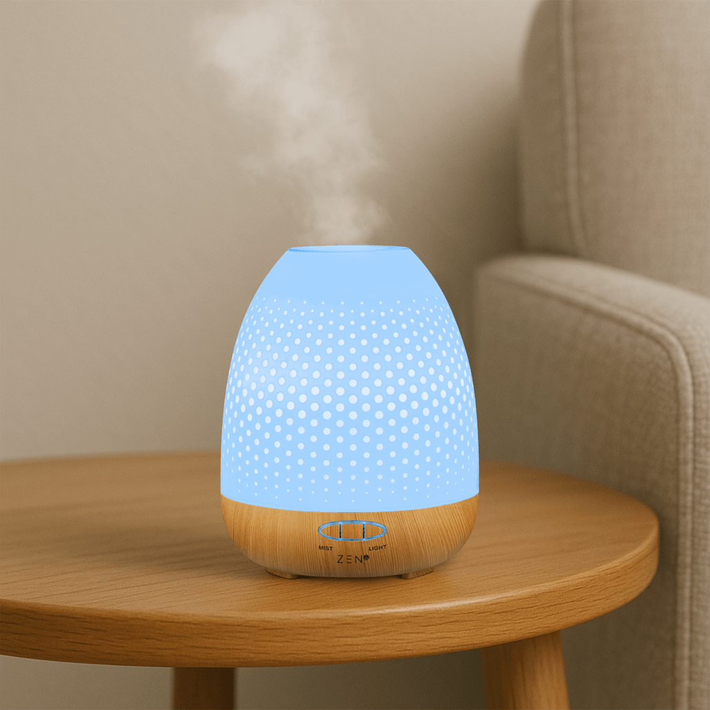 Zen Lunar Diffuser in white with blue light, emitting aromatic mist on a wooden table next to a cozy sofa.