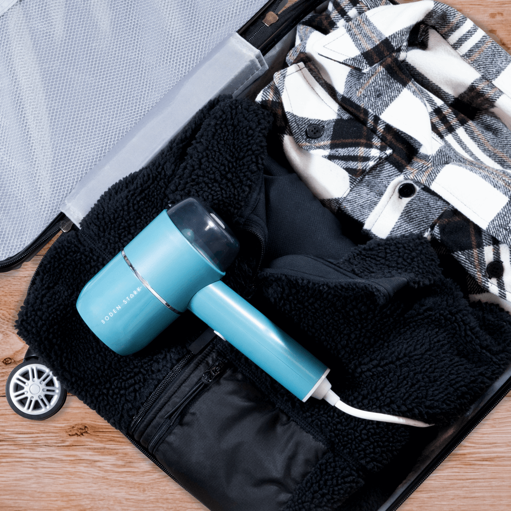 Boden Stark Handheld Steamer placed in a suitcase with a plaid shirt and black jacket.