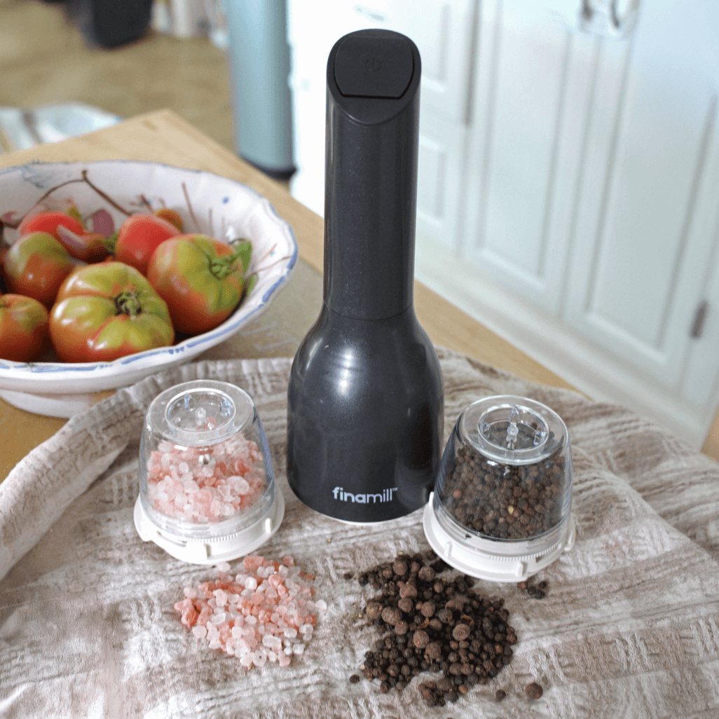 FINAMILL battery operated grinder in Midnight Black with salt and pepper containers, surrounded by fresh tomatoes.
