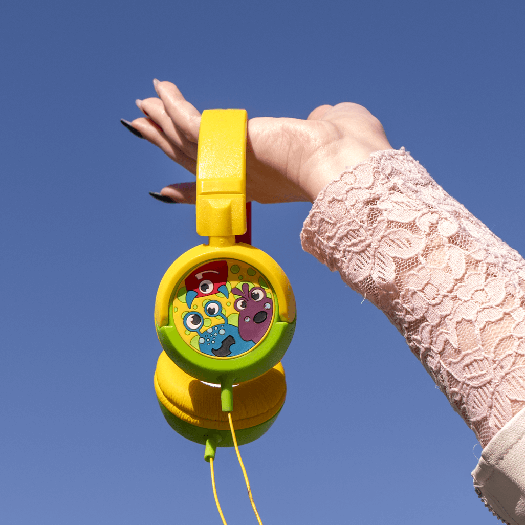 Hand holding vibrant yellow Amplify Kiddies Monsta Tunez Foldable Headphones with playful design against a blue sky.