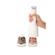 FINAMILL battery-operated grinder in soft cream with spices, hand holding the device next to spice containers.