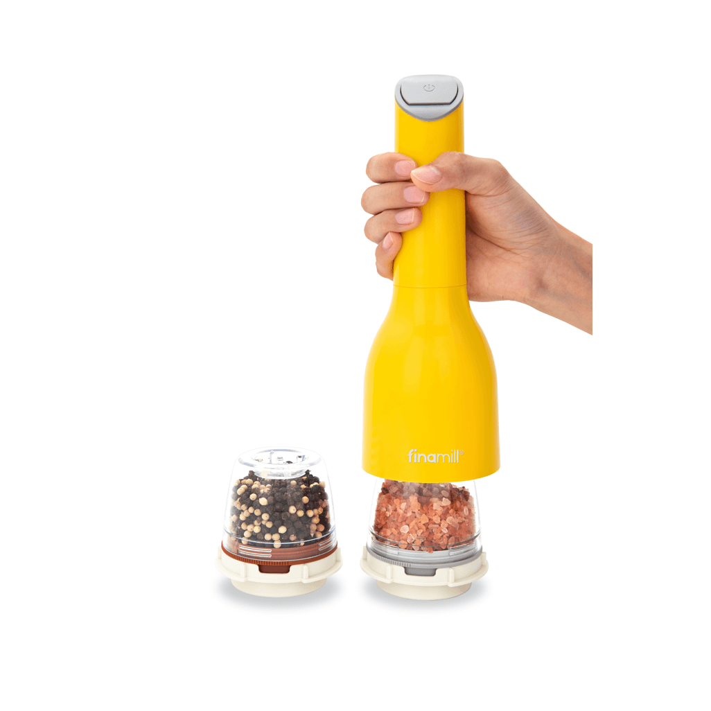 FINAMILL battery-operated grinder in Canary color, held in hand, with spice containers beside it.
