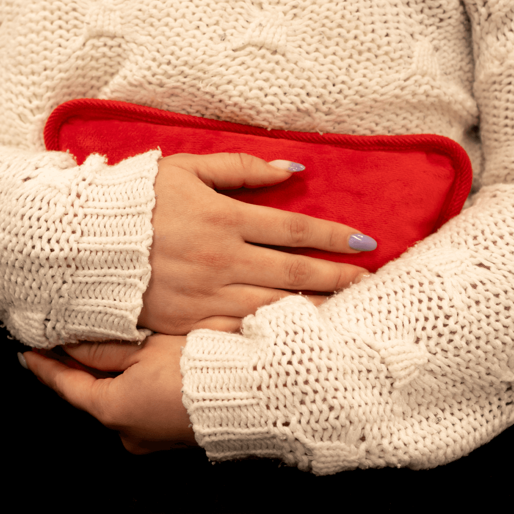 Person holding the ELEKTRA red hot water bottle in a cozy knitted sweater for warmth and comfort.