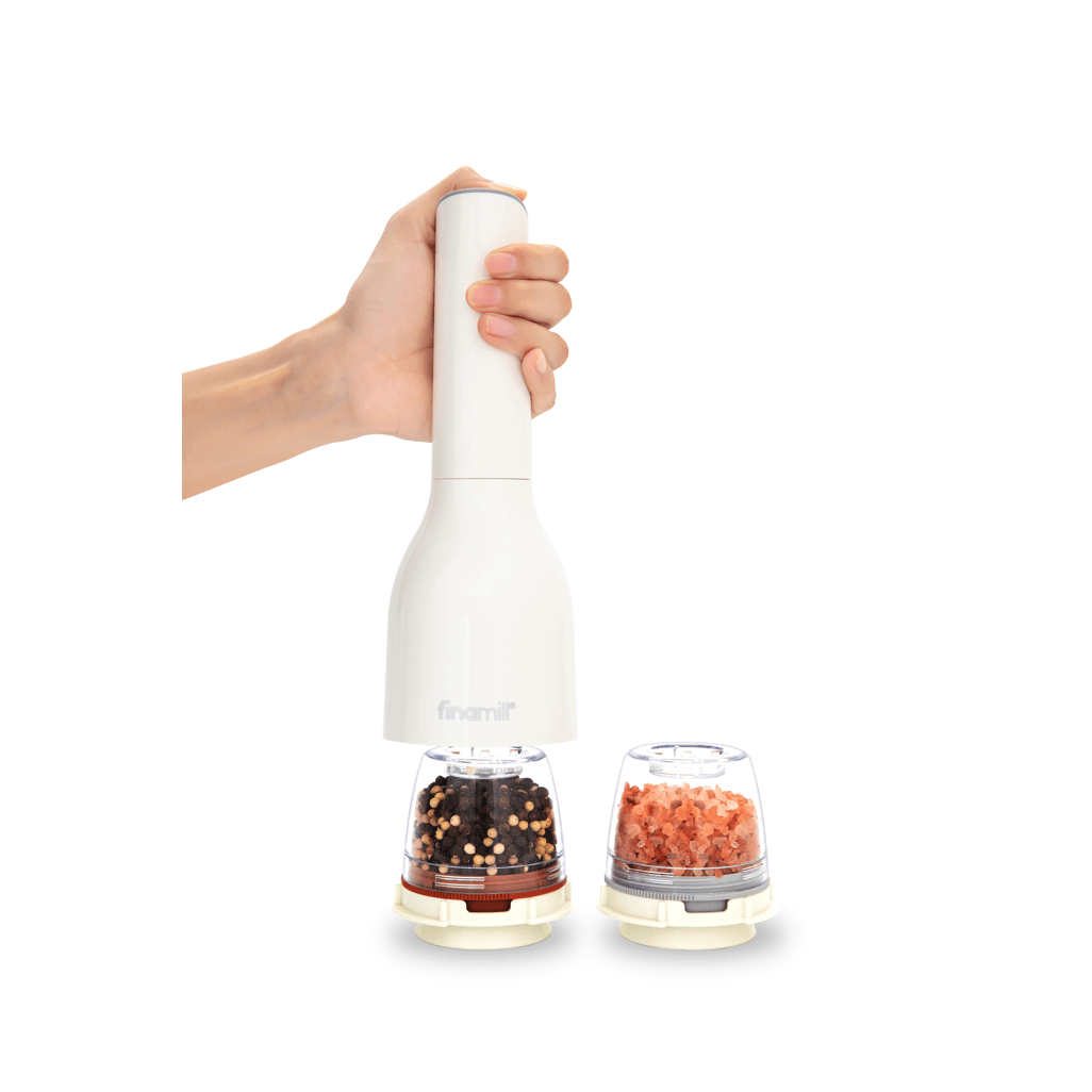 FINAMILL battery-operated grinder in soft cream, held by hand, with pepper and salt containers beside it.