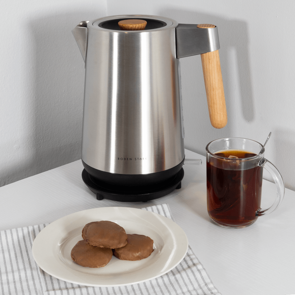 Boden Stark Anson Collection 1.7l 2000w stainless steel kettle with wooden handle, cookies, and tea on table.