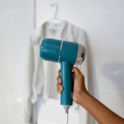 Boden Stark Handheld Steamer in teal color held against a backdrop of a white garment.