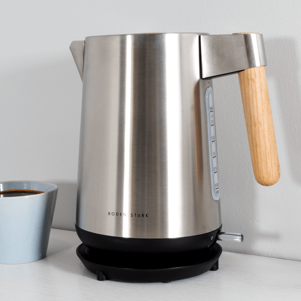 Boden Stark Anson Collection 1.7L 2000W stainless steel kettle with wooden handle next to a coffee cup.