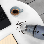 Boden Stark handheld vacuum cleaner on a table, cleaning coffee beans spilled near a laptop and a cup of coffee.