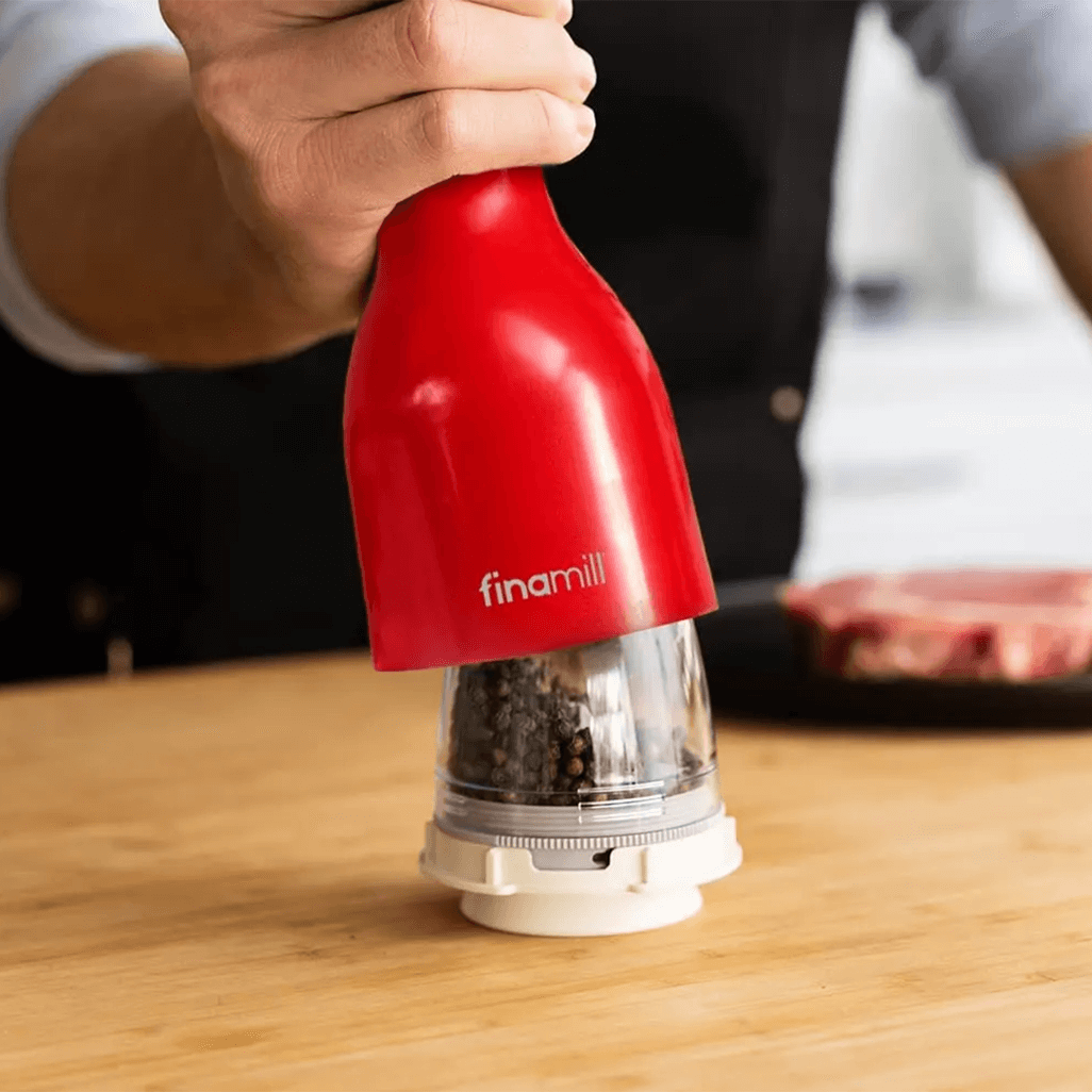 FINAMILL battery-operated grinder in vibrant red, used for grinding spices in a kitchen setting.