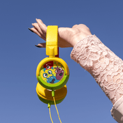 Hand holding vibrant yellow Amplify Kiddies Monsta Tunez Foldable Headphones with playful design against a blue sky.