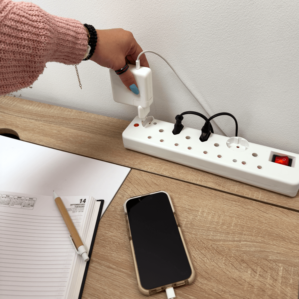 Hand plugging device into Ellies 8 Way Medium Surge Multiplug 0.5M on wooden desk with notebook and smartphone.
