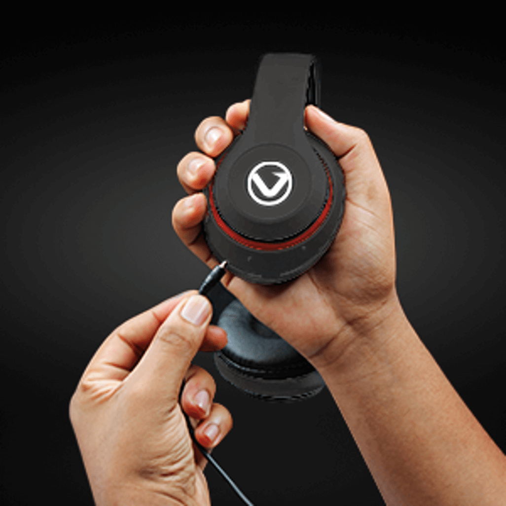 Person connecting cable to Volkano Impulse Series Bluetooth headphones - Black on a dark background.